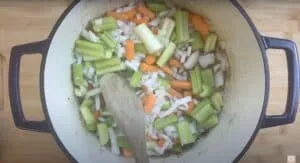 Chopped celery, carrots, and onions being sautéed in a large pot with a wooden spoon. Perfect for cozy soup recipes.